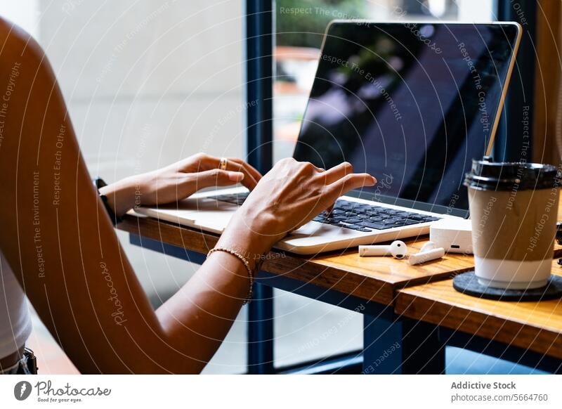 Cropped unrecognizable woman's hands typing on a laptop, with a coffee cup and smartphone on the table focused during remote work setting in Chiang Mai, Thailand