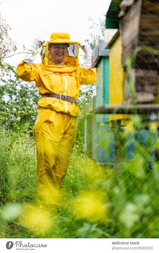 Positive mature woman beekeeper in yellow protective suit with veil and gloves standing and smiling in apiary smile overall happy cheerful lady positive nature