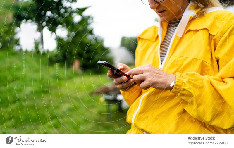 Focused cropped unrecognizable female Beekeeper in yellow overall using mobile phone while standing against green grass woman smartphone apiary beekeeper focus