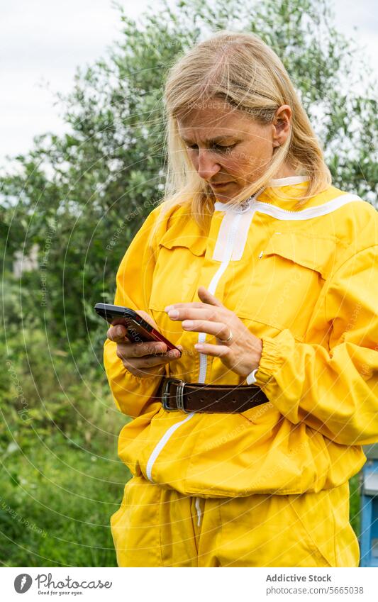 Concentrated mature woman with smartphone in apiary beekeeper overall mobile phone focus using gadget apiculture nature device concentrate female beehive