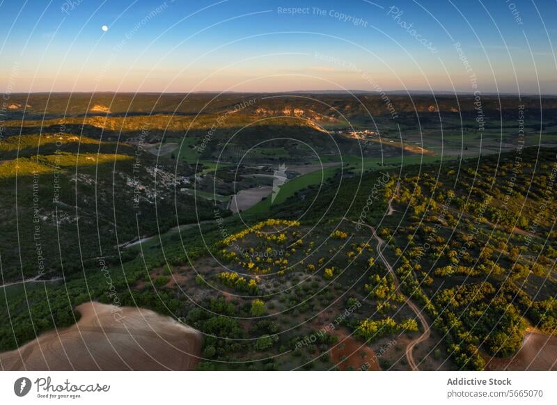 Twilight bathes the Alcarria landscape in golden hues as the moon rises over rolling hills dotted with lush greenery and cultivated fields Aerial Guadalajara