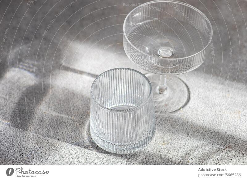 Elegant Glassware Casting Shadows on Textured Surface glass shadow light texture surface cocktail tumbler elegant crystal clear natural soft casting drinkware