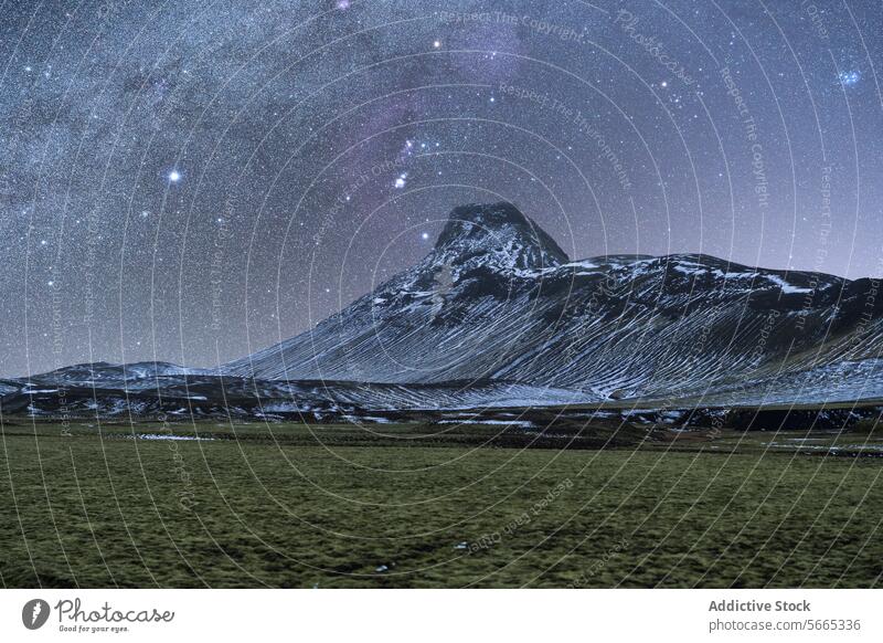 Star-studded night sky with the Milky Way over a snow-dusted mountain and grassy field in the Icelandic winter landscape nature stars outdoors galactic