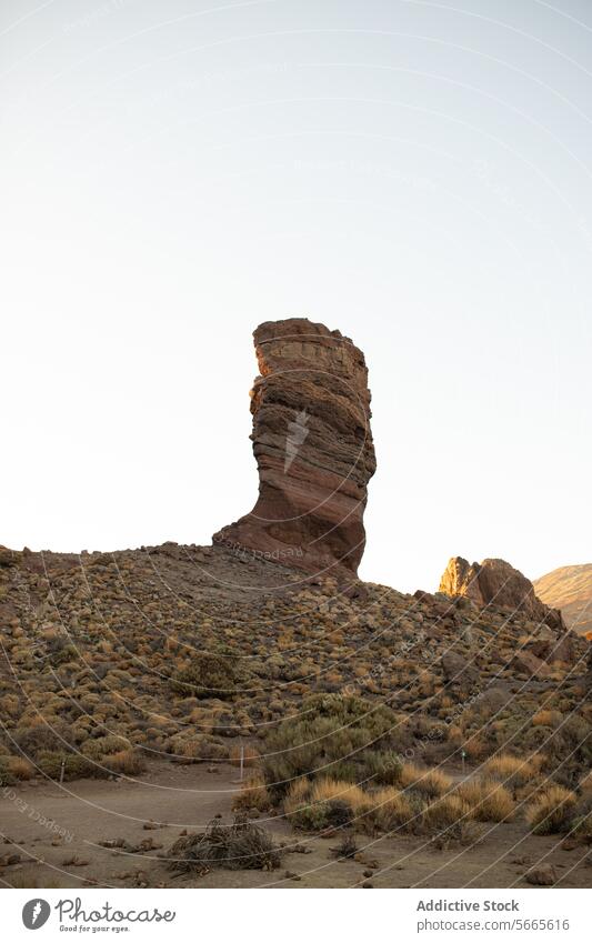 Majestic rock formation stands tall in a serene landscape pillar clear sky rugged terrain vegetation imposing natural outdoor geological landmark erosion