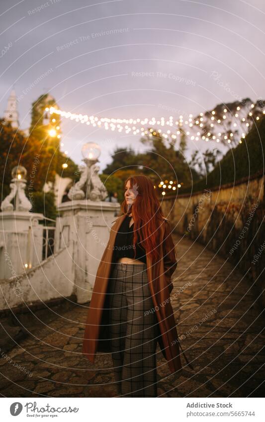 Elegant woman in autumn evening at historical plaza in Bogotá, Colombia red hair elegance style coat trousers stroll illuminated twinkle light dusk fashion