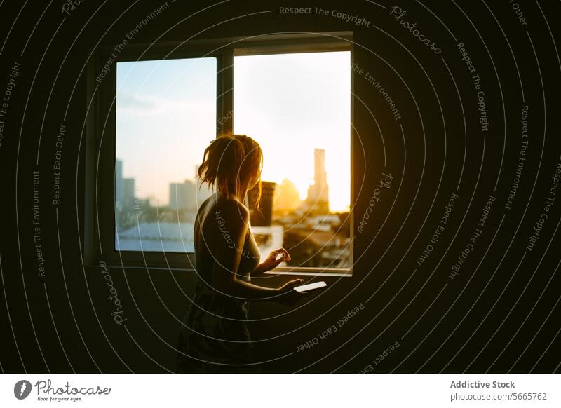 Woman contemplating cityscape through a window at sunset woman silhouette contemplation urban skyline glow warm sunlight standing gazing indoors peaceful