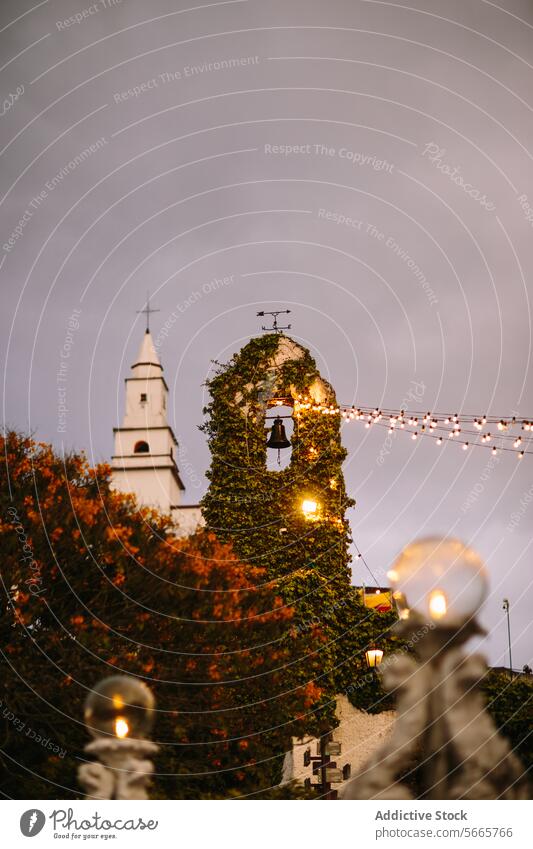 Church tower adorned with ivy and lights at dusk in Bogotá, Colombia twilight church lamp garland lights evening sky architecture outdoor autumn mood tranquil