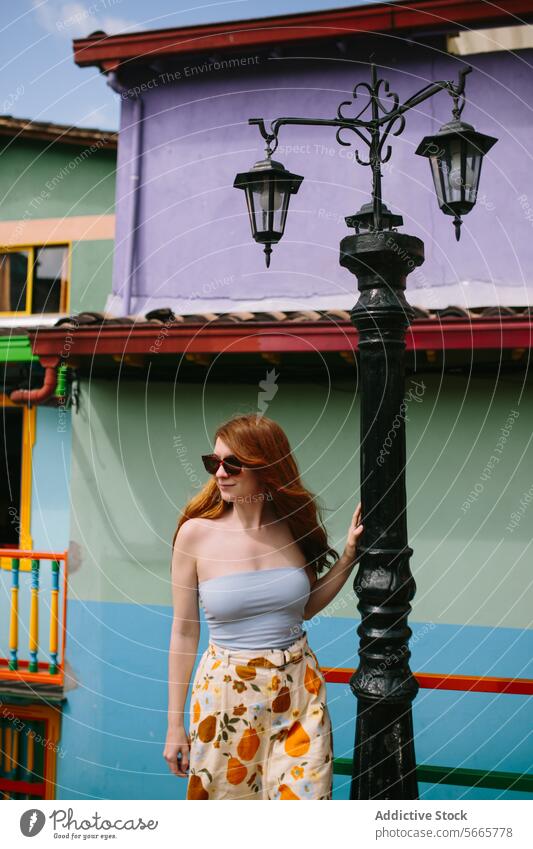 Fashionable woman posing by street lamp in vibrant setting in Guatapé fashion pose colorful building red hair sunglasses style outfit summer trendy skirt top