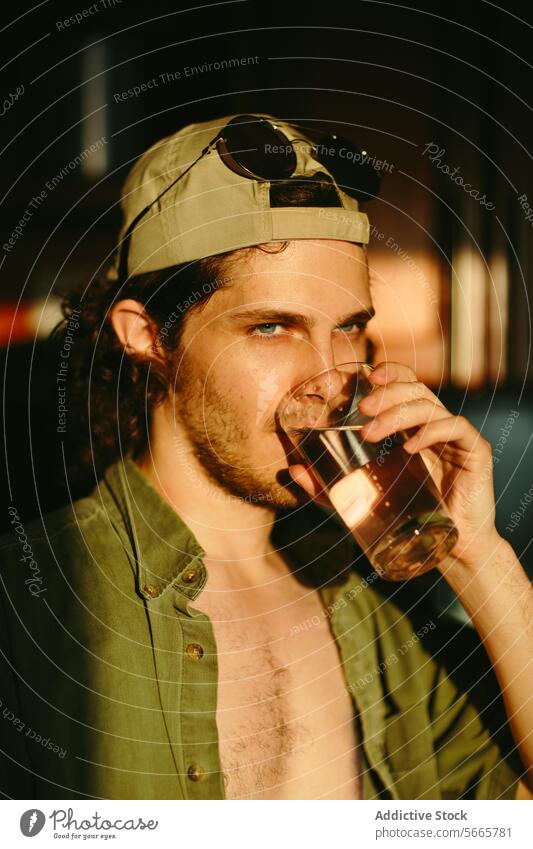 Young man enjoying a drink in warm sunlight young relaxed beverage adult male stylish casual cap sunglasses mood sipping leisure indoor thirst refreshment