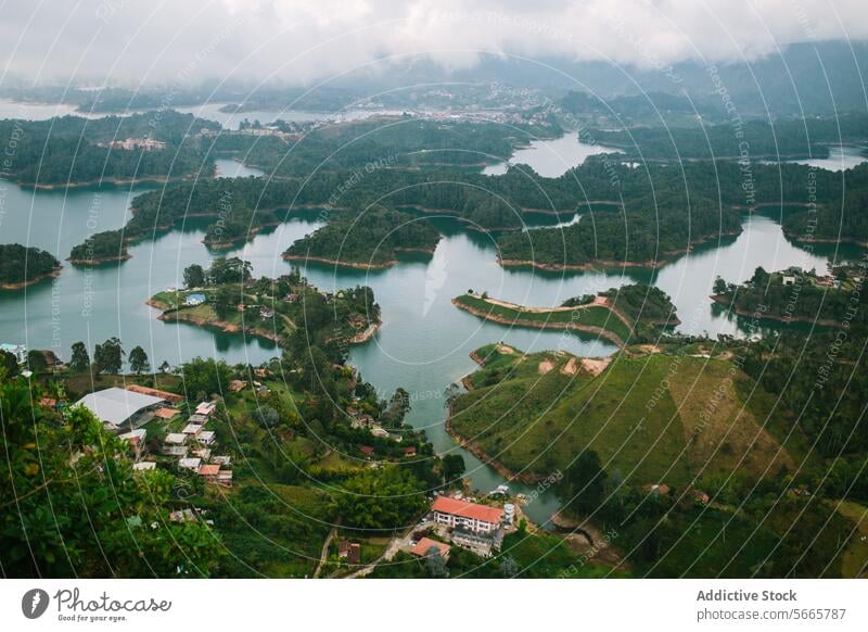 Misty lakeside landscape with lush greenery and settlements in Guatapé aerial view misty peninsulas forested hills serene water nature outdoor scenery