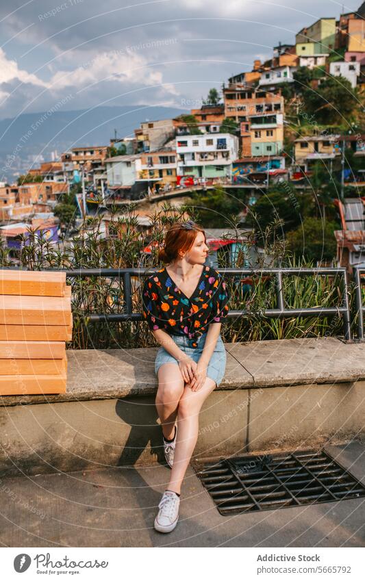 Young woman enjoying a scenic view of colorful houses in Medellin bench landscape hilly vibrant cloudy sky pensive young sitting urban travel tourism leisure