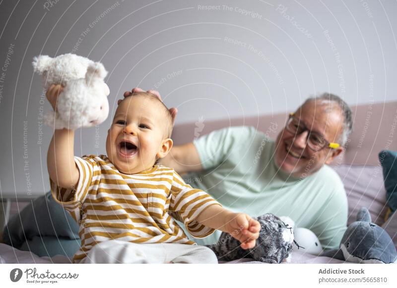 Grandfather and grandchild enjoy playful time together baby grandfather smile bed plush toy family happiness bonding togetherness playtime cheerful infant