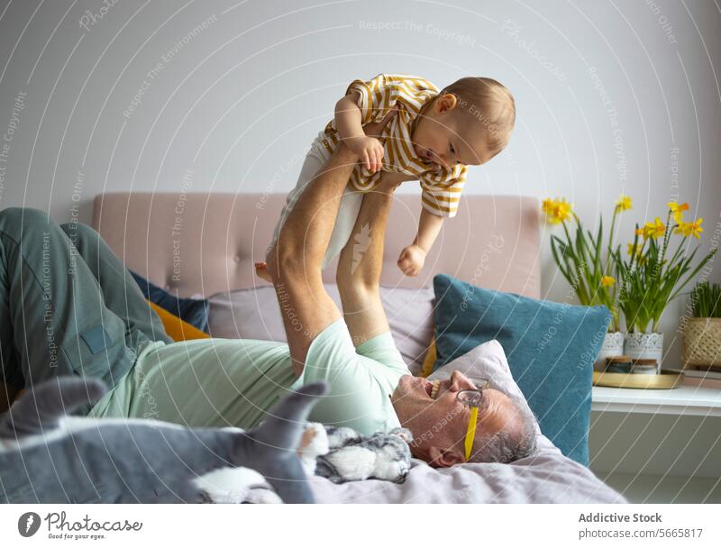 Grandfather and grandchild enjoying playful time indoors grandfather smile family bonding bedroom toddler happiness home interaction nurture care love lift