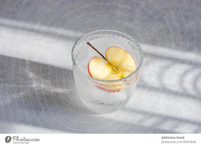 From above glass of tonic water with a slice of apple, with soft shadows and light textures in the background drink beverage refreshment bubbly effervescent