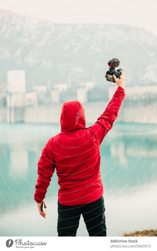 Back view person in a red hoodie taking a selfie with a camera in front of a tranquil lake and dam landscape photography outdoor water reflection hobby nature