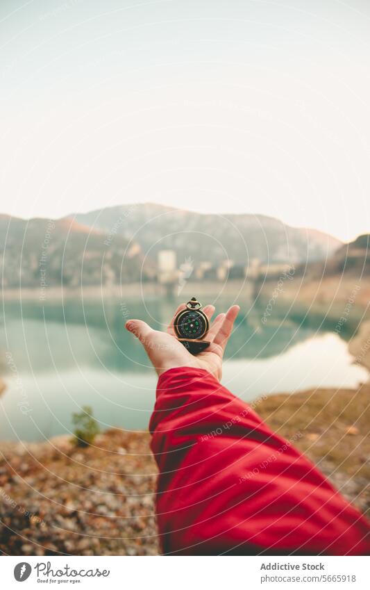 Anonymous hand holding a compass with a scenic lake and mountains in the background symbolizing guidance and exploration travel direction nature journey