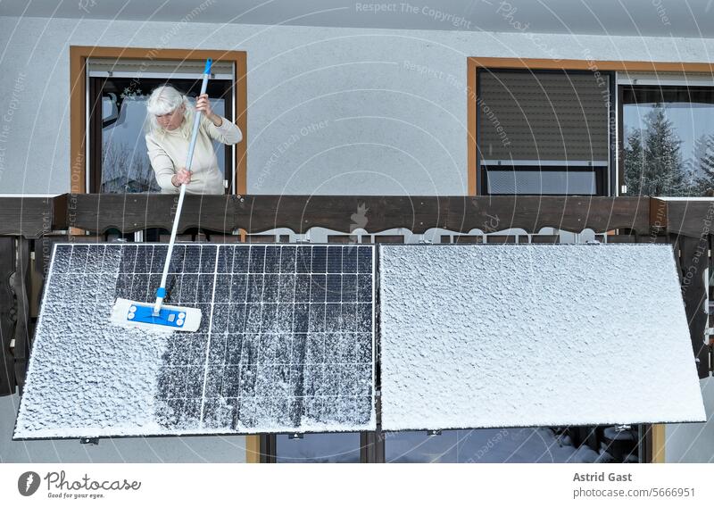 Eine Frau befreit im Winter ein Balkonkraftwerk vom Schnee balkonkraftwerk solar stromerzeugung frau winter schnee kehren säubern pflegen freiräumen