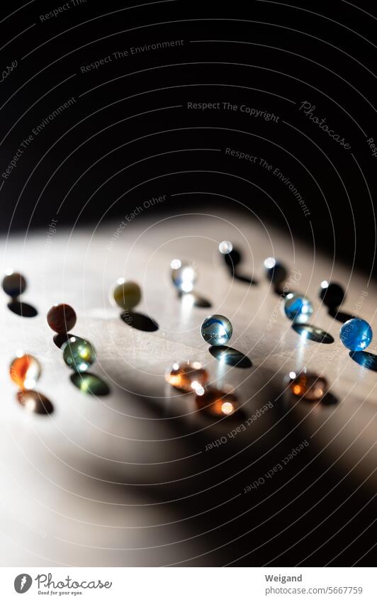 Many differently colored glass marbles on a wooden background, which are captured by a ray of sunlight, while the rest of the picture remains dark Marbles