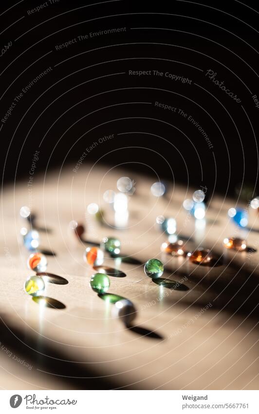 Many differently colored glass marbles on a wooden background, which are captured by a ray of sunlight, while the rest of the picture remains dark Marbles