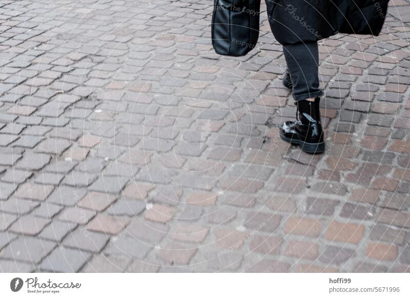 Partial shot of a person dressed in black walking on cobblestones from diagonally behind off Going black clothes Black Street urban garments Clothing