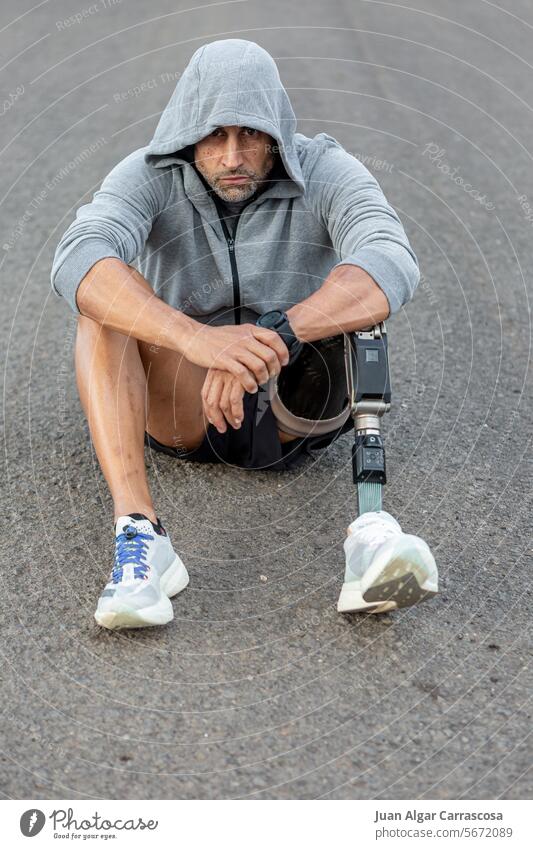 Handicapped male athlete sitting on asphalt road sportsman training handicap amputee prosthesis fitness unhappy break middle age mature wellness physical