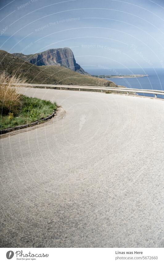 A remote road in Sicily is as beautiful as it gets, with the picturesque coastline of the small town of San Vito Lo Capo on the horizon. It's a wanderlust-inducing journey through Italy's island, showcasing the beauty of nature.