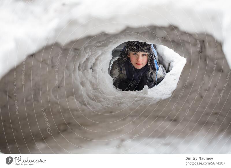Young boy hiding in a snow cave he made 12-13 years Igloo Looking At Camera Warm Clothing caucasian child cold cute deep fort fun game happy hide jacket kid