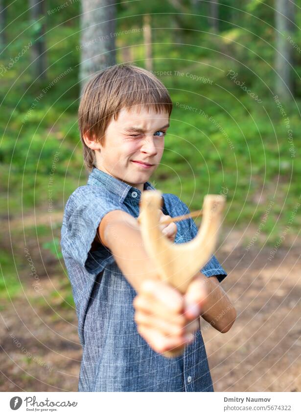 Boy aiming wooden slingshot outdoors accuracy activity arm bad bean shooter behavior boy brat caucasian child danger face flip fun game hand hand catapult