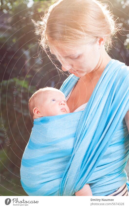 Young mother carrying her little baby girl in blue sling 0-6 months adult affectionate beautiful blanket bonding bright bundle care caucasian child childhood