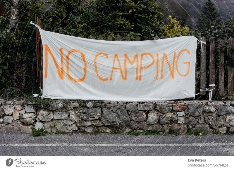 A flag with "No Camping" on it stands over a small wall in front of a garden fence no camping Caravan Nature Relaxation Camping site Tourism Summer vacation