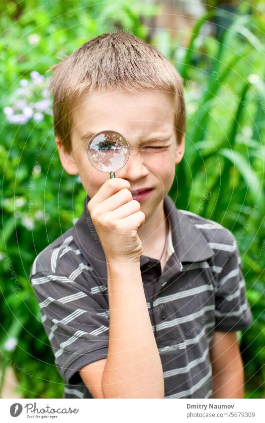 Young boy looking through hand magnifier outdoors 7 years caucasian child childhood closed discover education environment exploration eye garden glass hold kid
