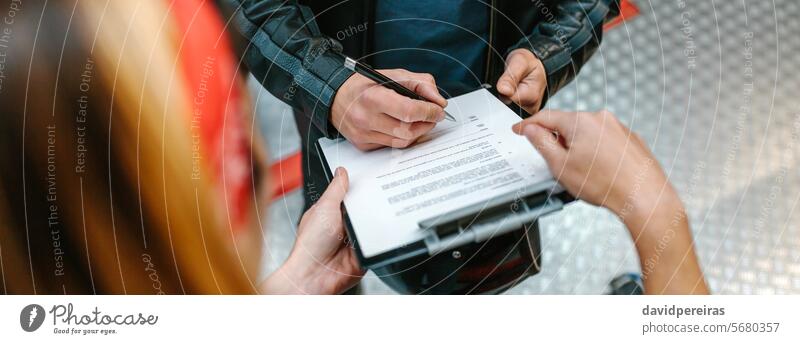 Female mechanic holding clipboard while biker man signing insurance policy on workshop unrecognizable female document agreement hands pen motorcycle motorbike