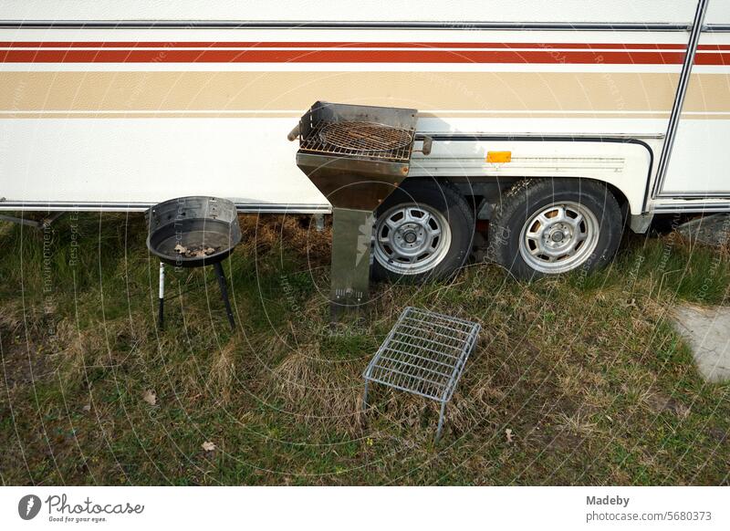 Camping grill and charcoal grill in front of a caravan with tandem tires for vanlife and camping on the campsite at the Oerlinghausen glider airfield near Bielefeld in the Teutoburg Forest in East Westphalia