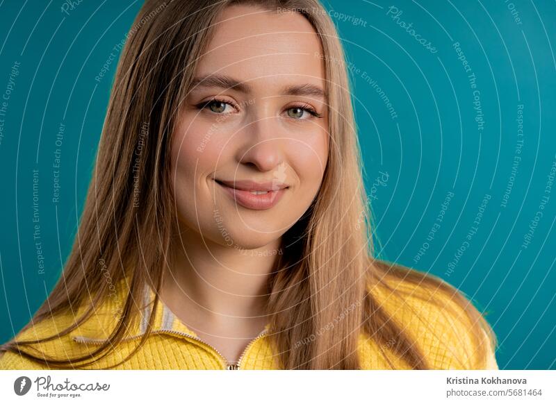 Young pretty woman in yellow sweater looking to camera on blue background. Face. acting afraid amazement amusing beautiful beauty beige breath brunette