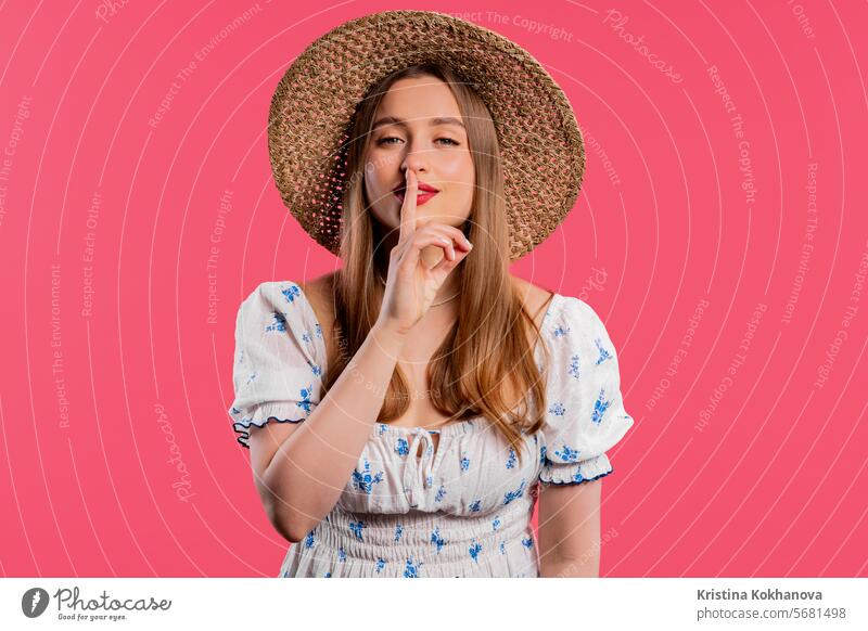 Smiling pretty woman with finger on lips - shhh, secret, silence, pink studio asking background between you and me biting businesswoman charming closeup concept