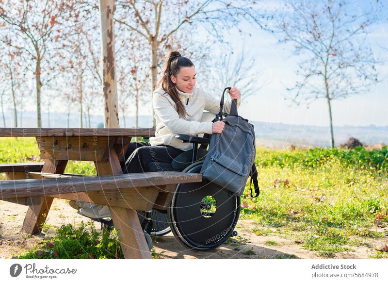 A young woman in a wheelchair organizing her backpack at a park table Woman outdoor casual wear sitting female daytime accessibility personal item recreation