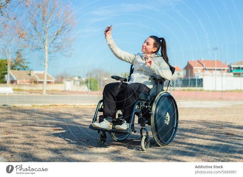 A young happy woman in a wheelchair taking a selfie with her smartphone in the park Woman outdoor photography casual wear sitting female daytime technology