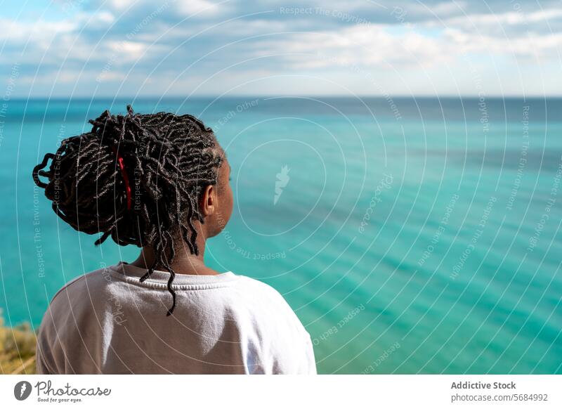 Anonymous African american woman peacefully looking away at turquoise sea during solo travel tranquil contemplative ocean thoughtful african american pensive