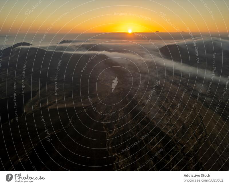 The sun rises above the horizon, casting a warm glow over the misty mountains of Fuerteventura sunrise aerial landscape dawn light nature scenic tranquil beauty