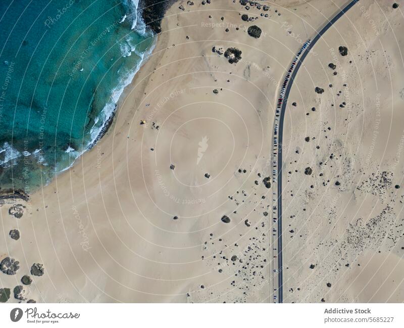 Aerial view of a single winding road cutting through the expansive Corralejo Dunes with the azure ocean gently lapping the shore in Fuerteventura dunes sandy