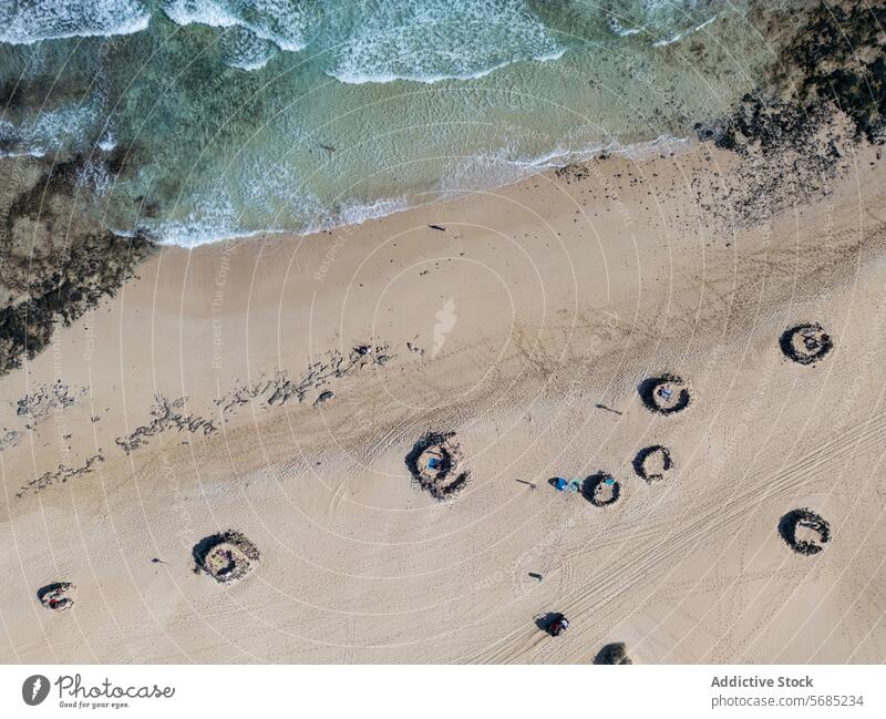Overhead shot of unique spiral rock formations on the Corralejo Dunes with waves washing ashore in Fuerteventura Aerial view beach ocean sand nature texture