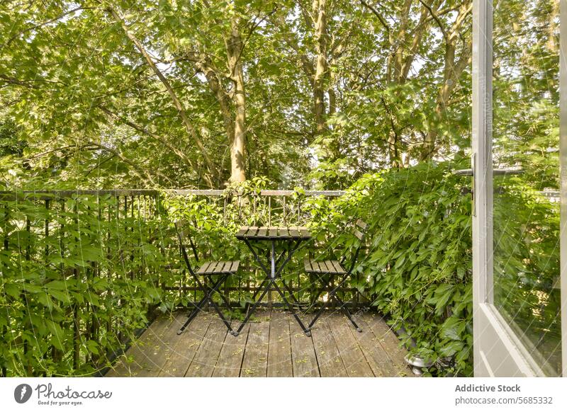 Cozy balcony setting surrounded by lush greenery table chair plant tree urban escape serene tranquil black metal outdoor furniture deck foliage wooden floor