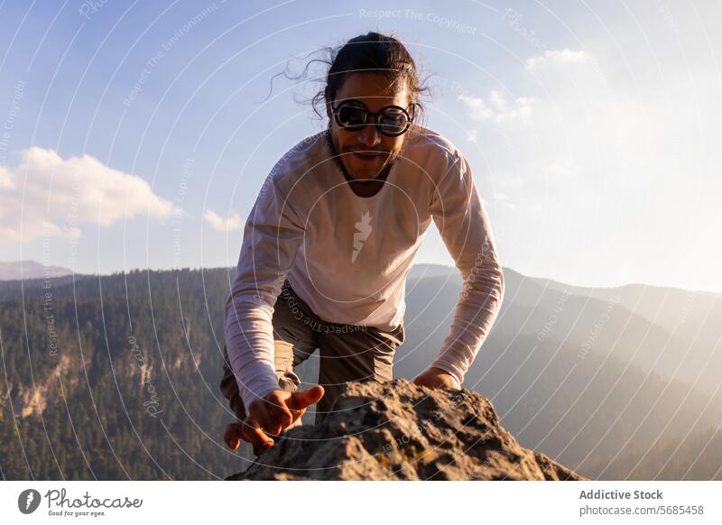 Brave young man climbing mountain cliff ridge positive brave sunglasses style cloth nature adventure highland travel male smile cheerful rough range happy