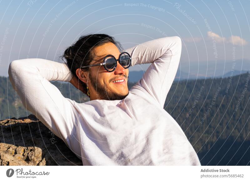 Cheerful young man resting on rocky mountain happy sunglasses enjoy nature cheerful toothy smile style brunet travel male positive carefree glad ridge guy