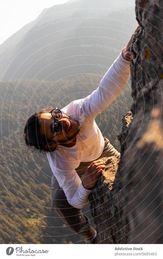 Brave young man climbing mountain cliff ridge positive brave sunglasses style cloth nature adventure highland travel male smile cheerful rough range happy