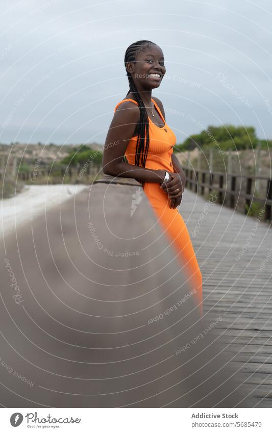 Happy African American woman standing on foot bridge happy smile boardwalk gown lean braid railing lady appearance positive female african american casual