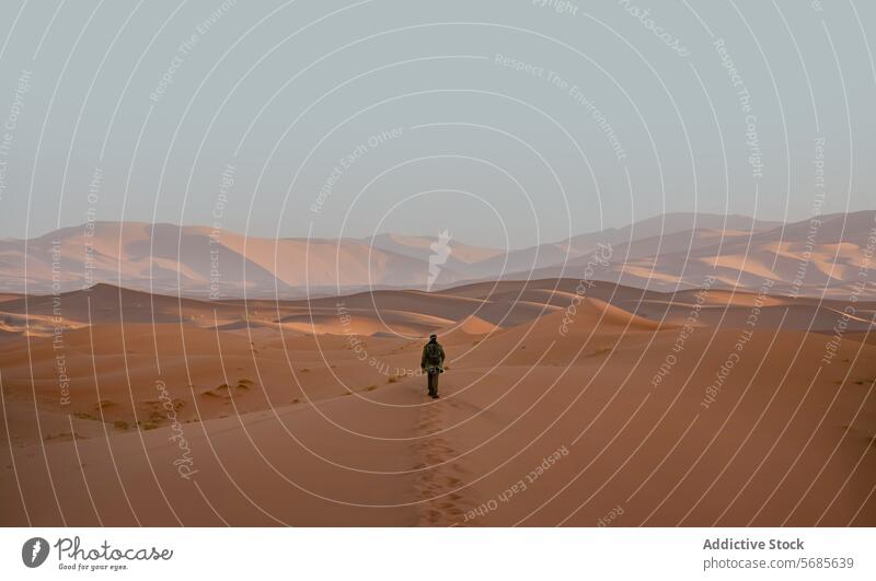 Lone anonymous traveler trekking across the Merzouga Desert in Morocco merzouga desert morocco sand dune adventure solitary figure sunset moroccan erg chebbi