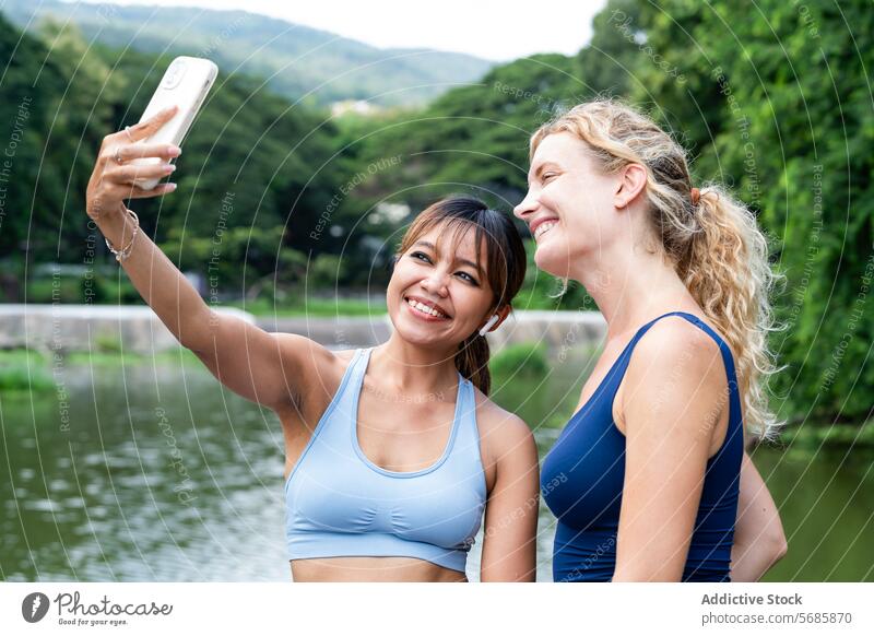 Happy women taking selfie near pond cheerful sportswomen smartphone self portrait break activewear happy mountain training friend sportswear fitness healthy