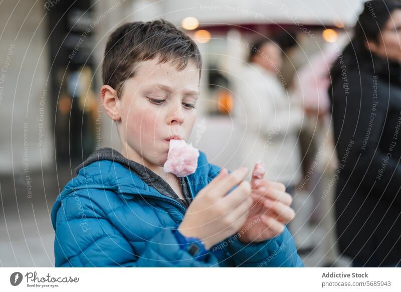 A focused young boy enjoying a bite of pink cotton candy in a busy urban blurred background setting sweet snack treat dessert sugary spun fluffy indulgence