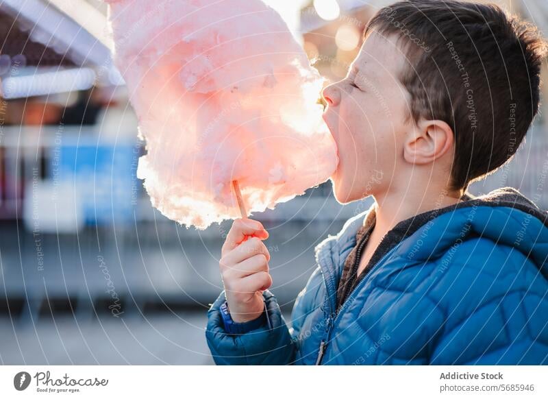 Side view of delighted young boy in a blue jacket with eyes closed biting huge cotton candy at an amusement park bite treat sweet fluffy outdoor child sugary